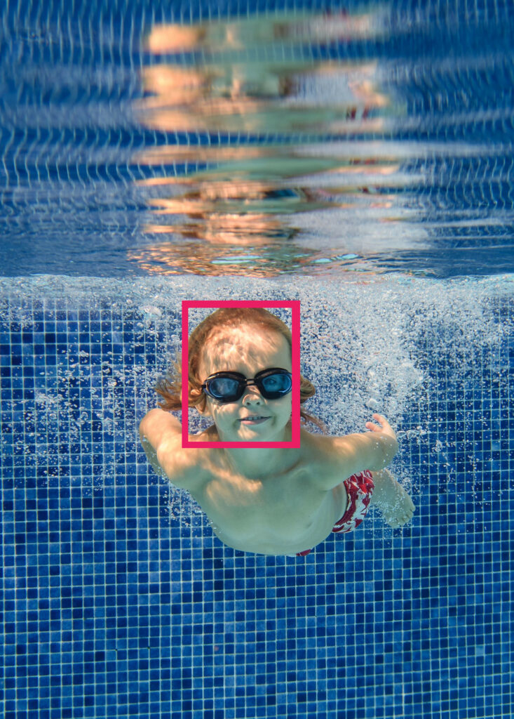 Usměvavý chlapec plave pod vodou v bazénu